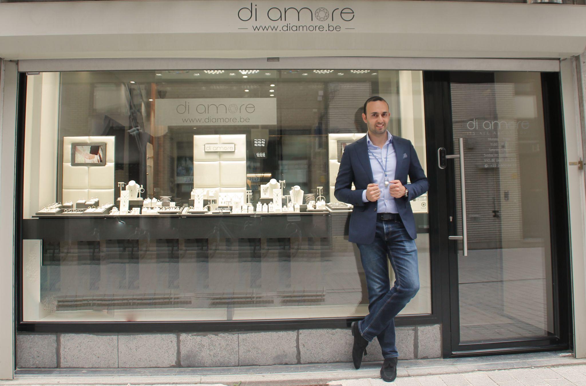Owner of Di Amore jewelry store standing in front of the shop's window display, featuring elegant jewelry pieces, with the Di Amore logo visible above the storefront.