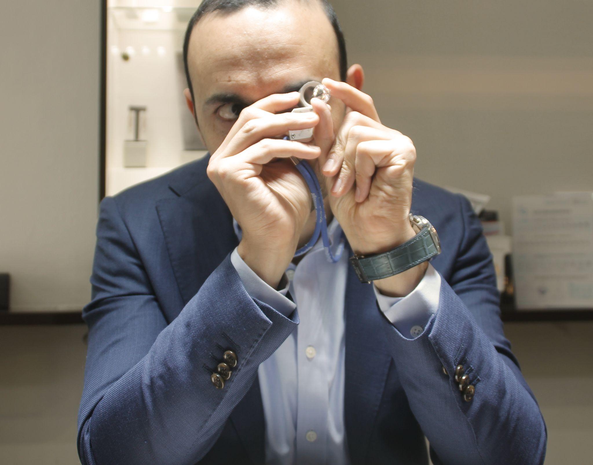 Jeweler closely inspecting a diamond ring with a loupe, wearing a blue suit and focusing intently on the gemstone.