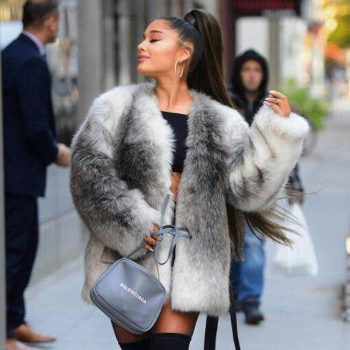 Stylish woman with long hair in a high ponytail wearing a gray fur coat, black crop top, thigh-high black boots, and carrying a gray Balenciaga handbag, walking confidently on a city street