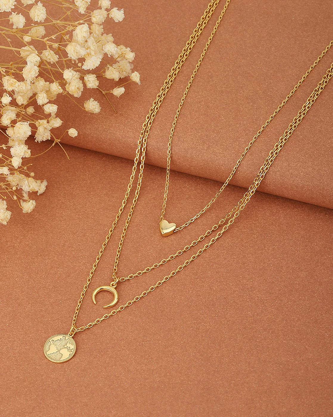 gold necklace with heart, crescent moon, and world map pendants on a brown background,
