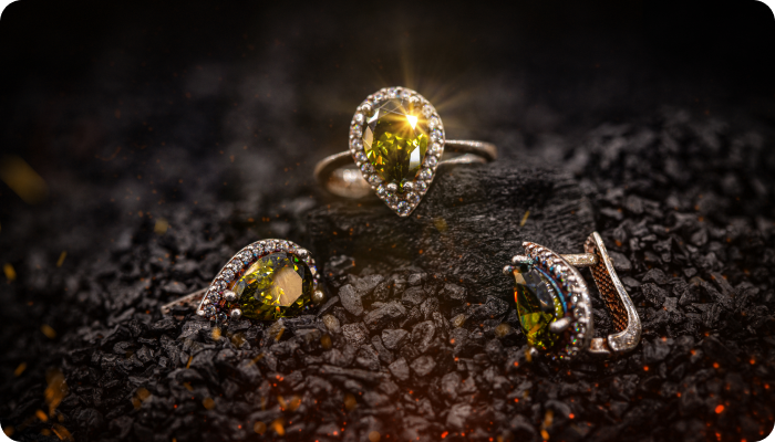 Elegant jewelry set with pear-shaped green gemstones and diamond halos on dark textured surface