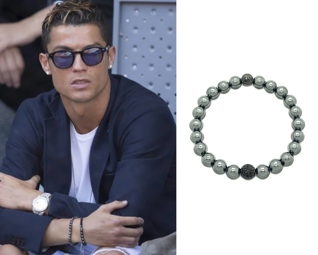 Man wearing sunglasses, a navy blazer, and a white shirt, accessorized with a silver watch and black bead bracelet, sitting with arms crossed; next to a close-up image of a black bead bracelet with a central decorative bead.