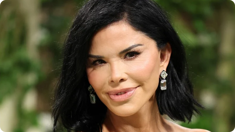 A woman with shoulder-length black hair is wearing elegant drop earrings and has a warm, confident smile. The background features a soft-focus green and natural setting, highlighting her radiant appearance.