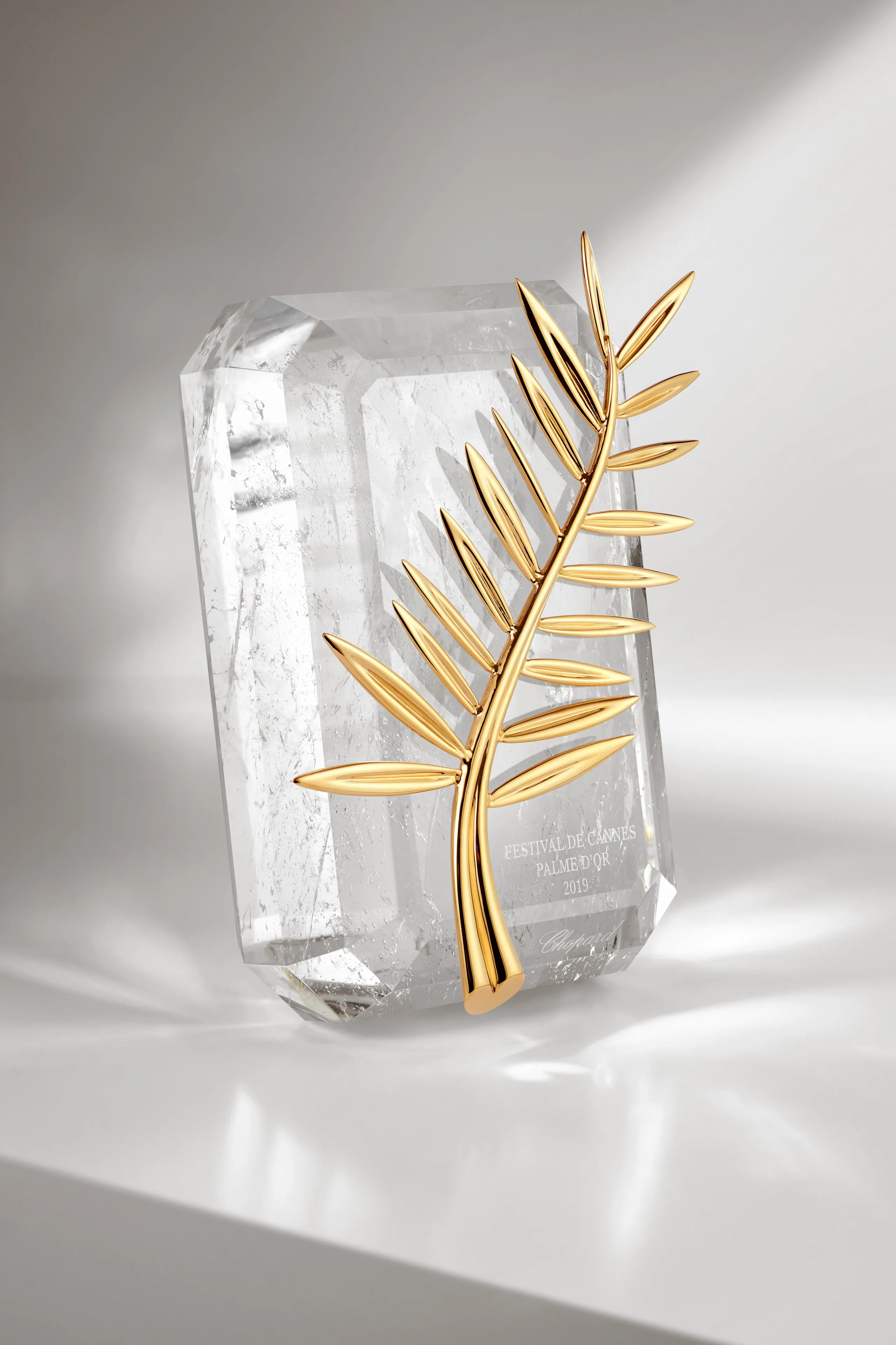 Palme d'Or trophy with a crystal base and golden palm leaf, presented at the Cannes Film Festival, against a simple and well-lit background.