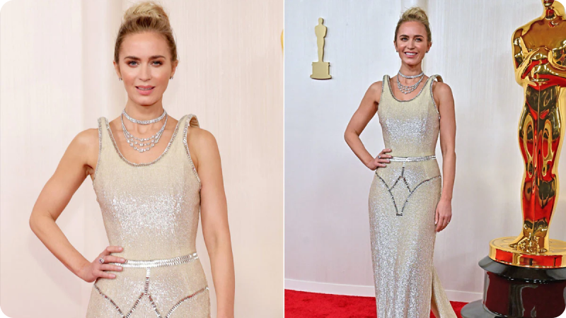 Emily Blunt wearing a sparkling silver gown and layered necklaces, posing at an event or awards ceremony with Oscar statuettes in the background.