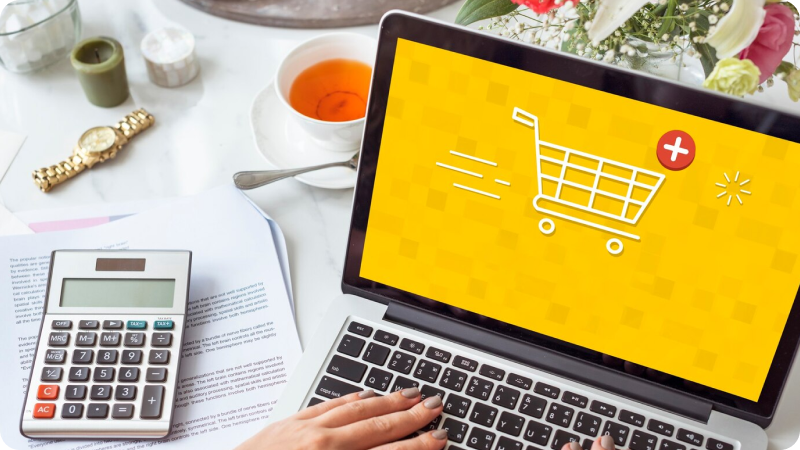 Laptop showing shopping cart icon, calculator and tea nearby.