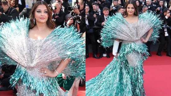 Aishwarya rai Woman on the red carpet wearing a glamorous silver and teal metallic fringed gown with a dramatic wide collar and long flowing train, with photographers in the background.