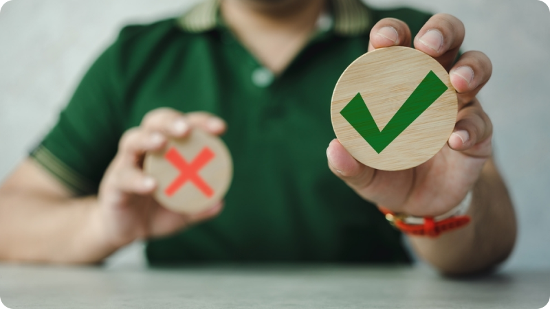 Person holding a wooden circle with a green check mark in one hand and a wooden circle with a red cross in the other hand, symbolizing approval and disapproval.